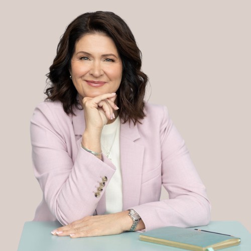 Tiina Kuusisto vaaleassa jakussa, hymyillen pöydän ääressä